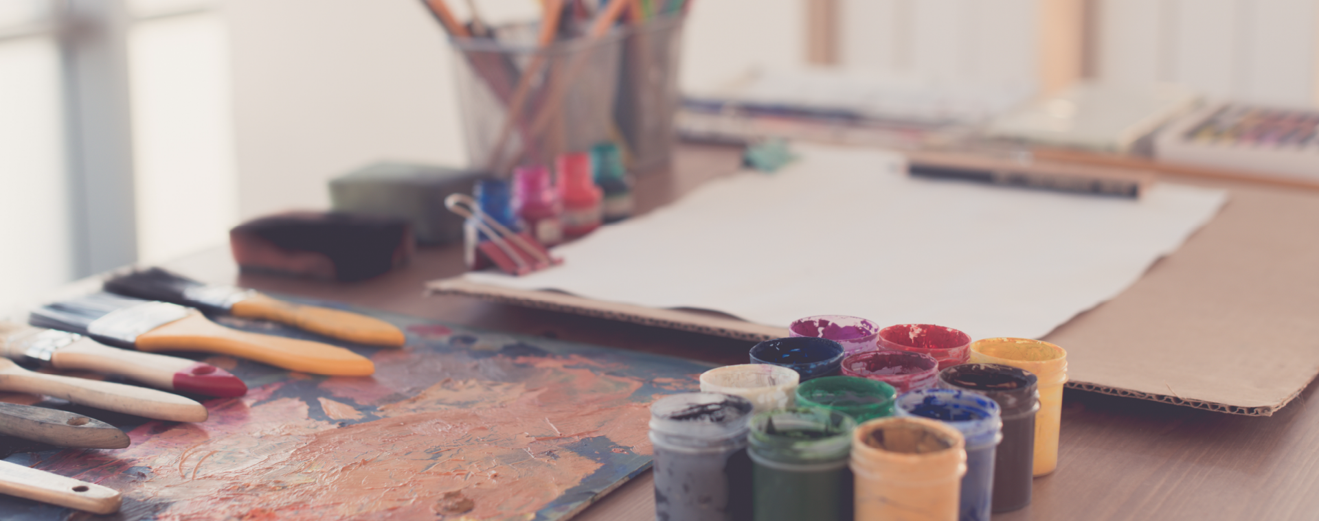 An image of an artist studio with paints, paintbrushes and canvas boards which is meant to represent us at work in our studios making great things for you.